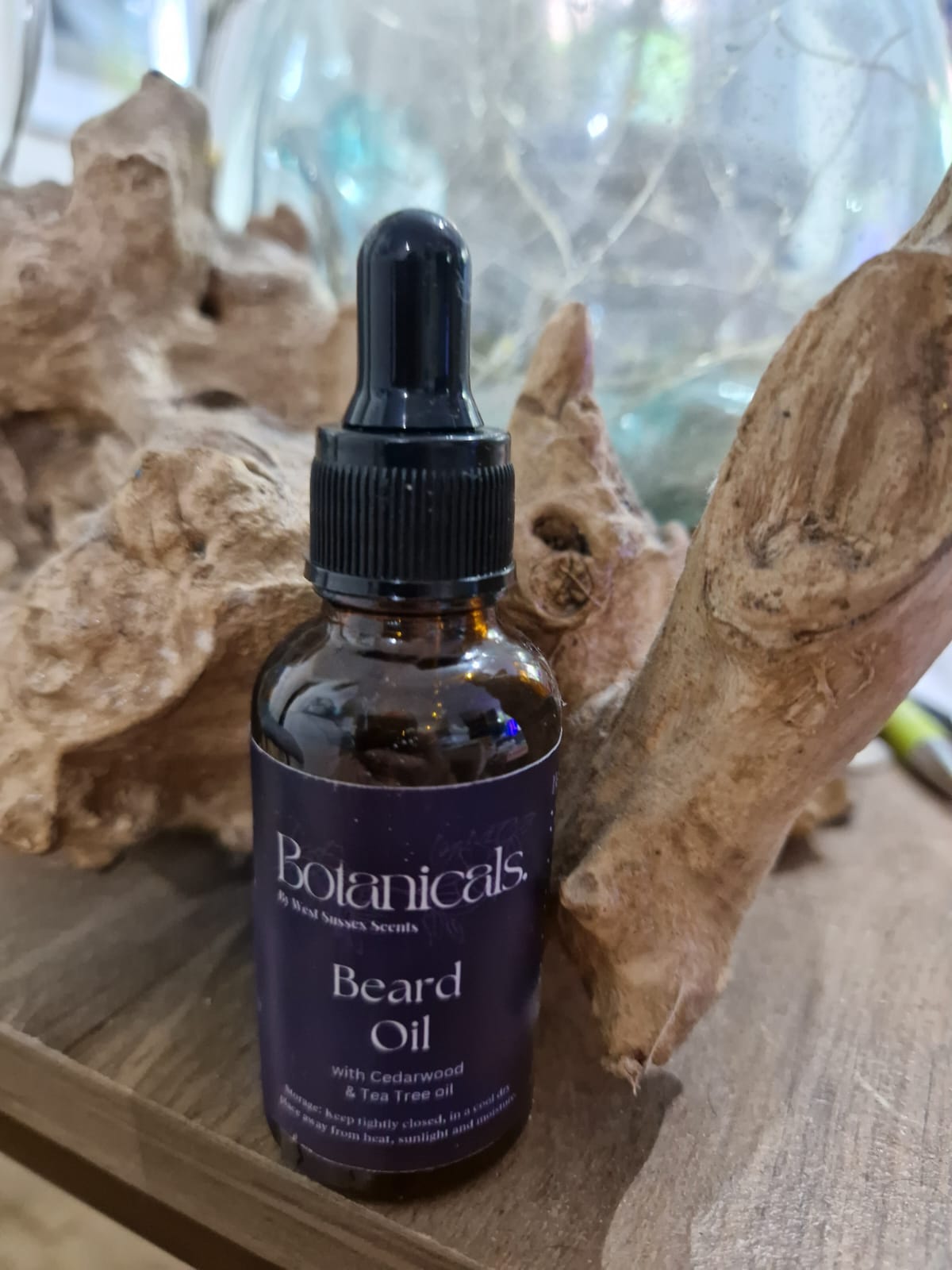 Bottle of Botanicals beard oil with a dropper on a wooden surface with natural elements.