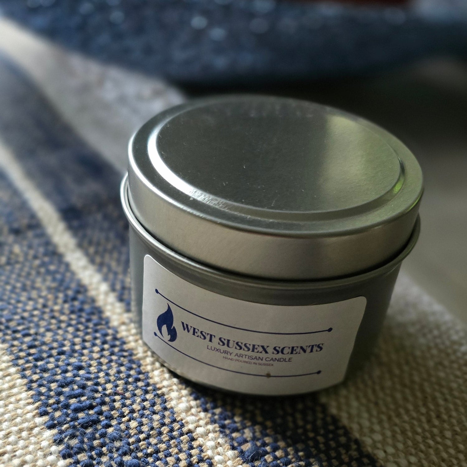 Small cylindrical silver tin container with a label on a textured fabric surface